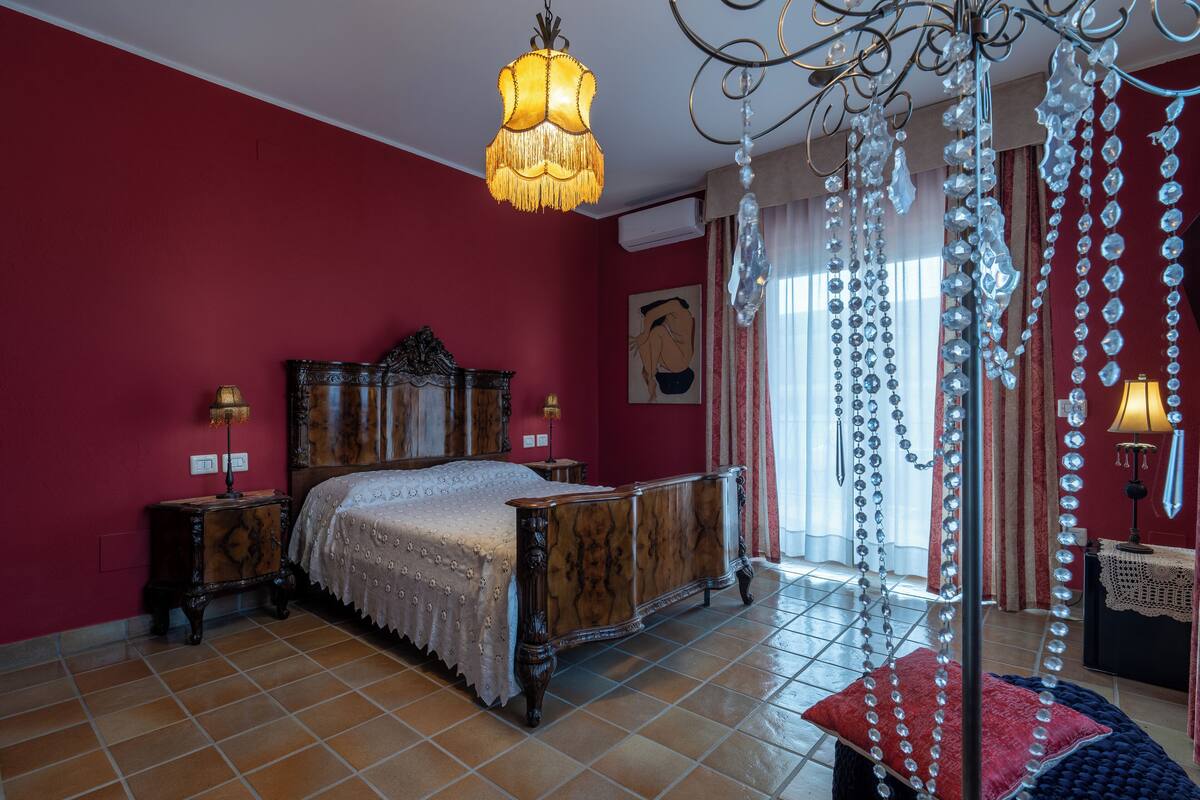 A bedroom with a wooden bed, a chandelier, and a red wall.