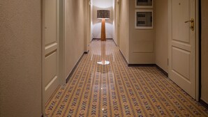 Ein Hotelgang mit gemustertem Teppich, weißen Türen und einer wandmontierten Leuchte.