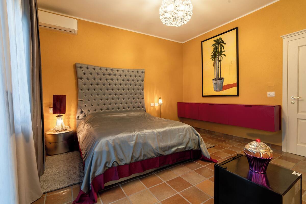 A bedroom with a large bed, a red nightstand, a wall-mounted TV, and a door.