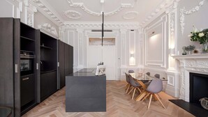 Una cocina moderna con muebles oscuros, una isla central y un comedor con sillas y una mesa.