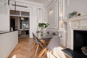 A dining area with a glass table, grey chairs, and a white fireplace.