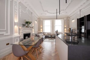 A spacious living area with a glass dining table, sofas, and a fireplace.