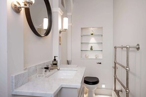 A bathroom with two sinks, a toilet, a mirror, and a glass shelf unit.