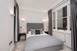 A neatly arranged bedroom with a large bed, bedside tables, and a window with curtains.
