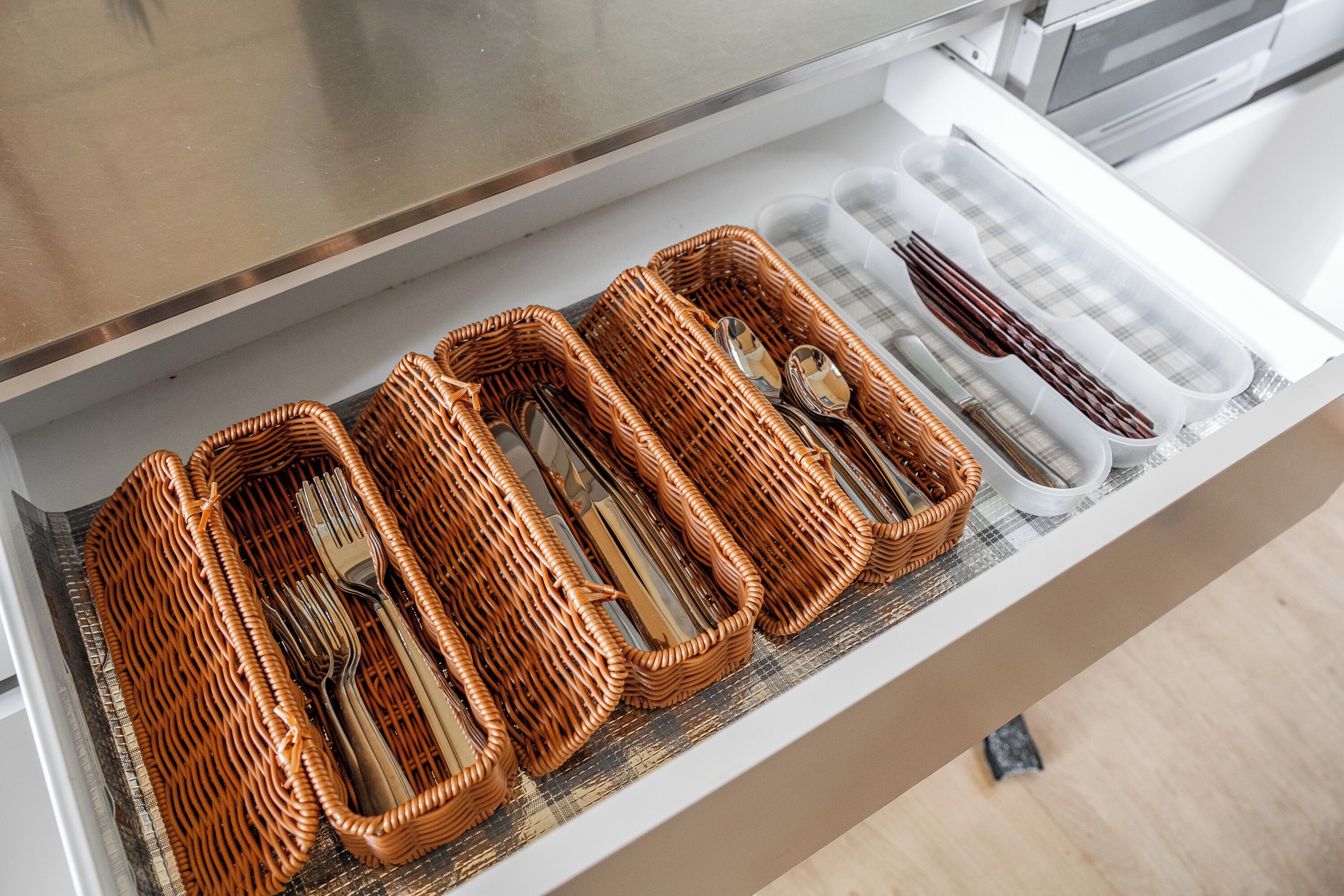 A drawer with wicker baskets containing cutlery.