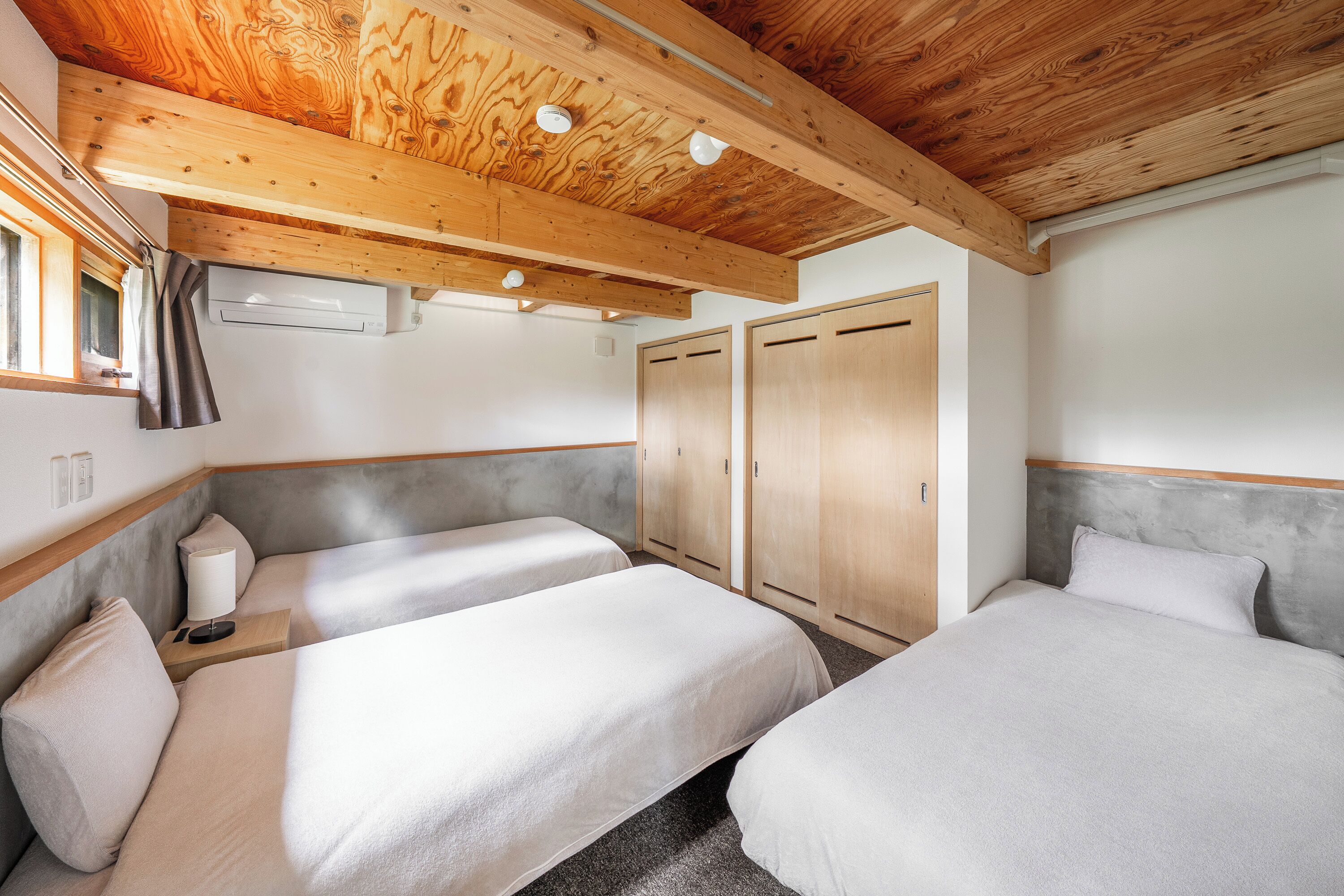 A bedroom with two beds, wooden ceiling beams, a wardrobe, and a window with curtains.