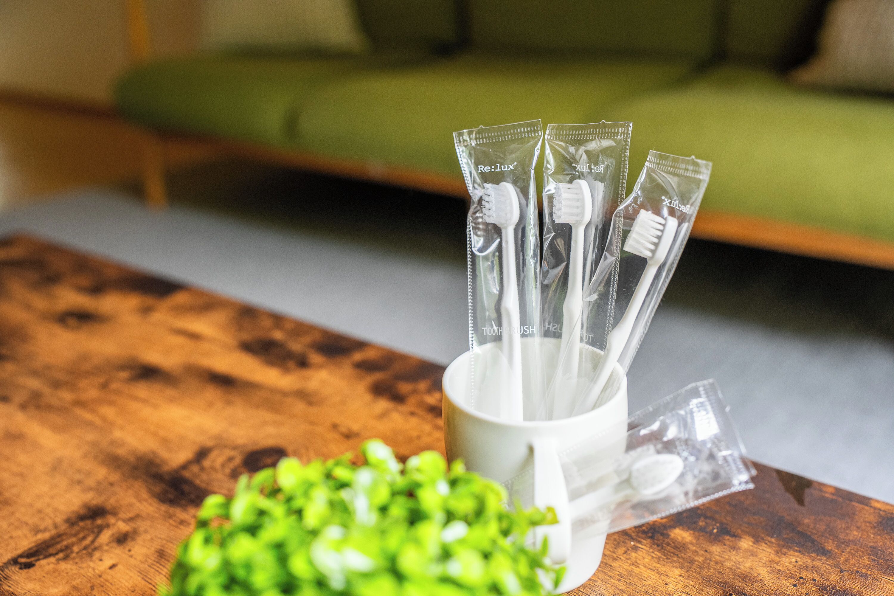 A white mug with toothbrushes in clear tubes on a wooden table.
