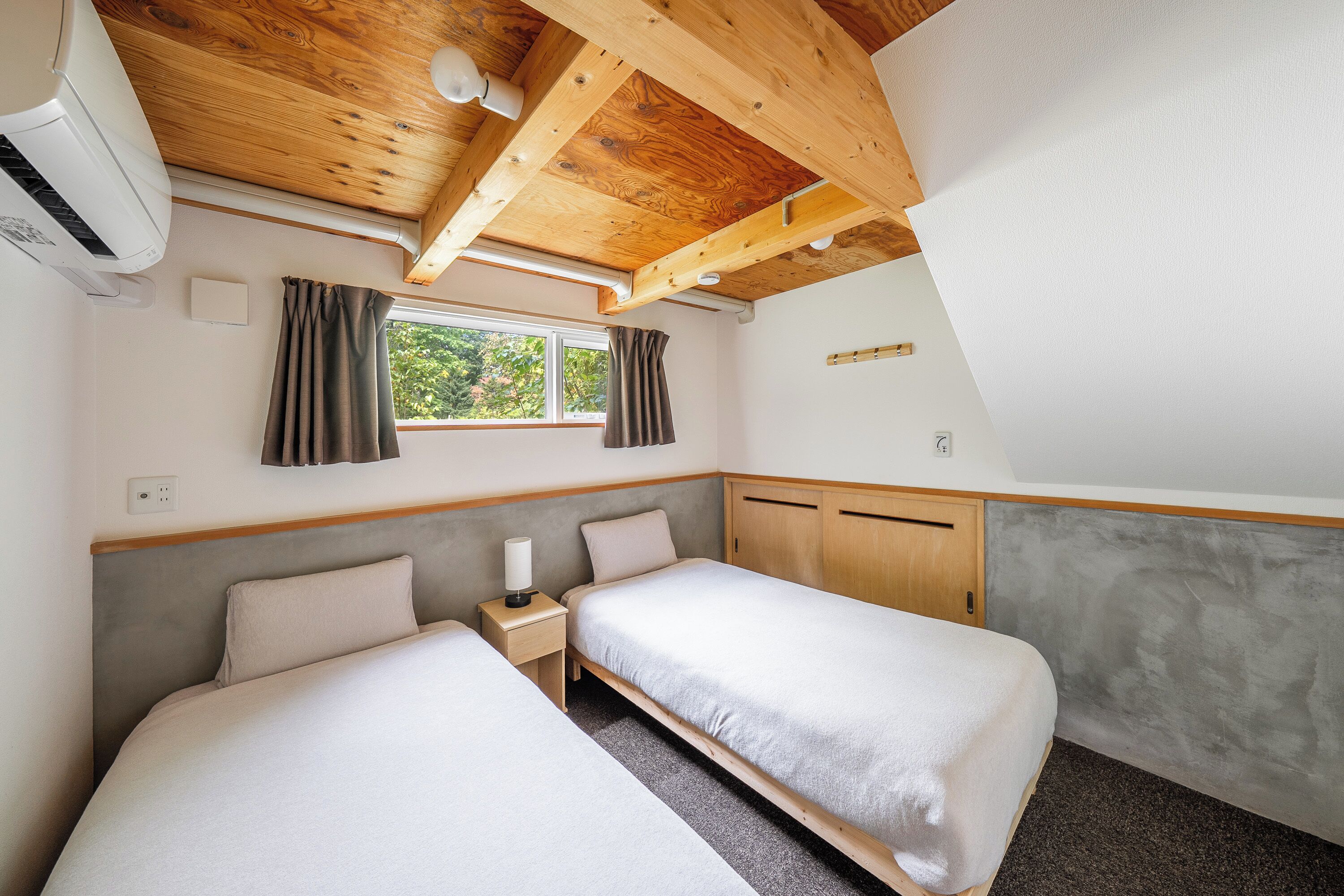 Una camera da letto con due letti, una finestra, travi a vista in legno e una parete grigia.