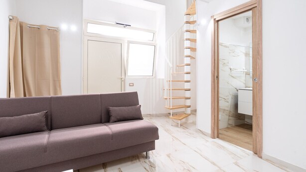 A modern living room with a sofa, a staircase, and a bathroom visible through an open door. - Mifra n 1 in Bari With 1 Bedrooms and 1 Bathrooms (Bari)