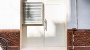 A white door with a window and a metal grill, a brown textured wall, and a white pipe. - Mifra n 1 in Bari With 1 Bedrooms and 1 Bathrooms (Bari)