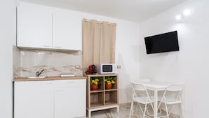 A compact kitchen with white cabinets, a microwave, a small shelf with potted plants, and a dining area with white chairs. - Mifra n 1 in Bari With 1 Bedrooms and 1 Bathrooms (Bari)