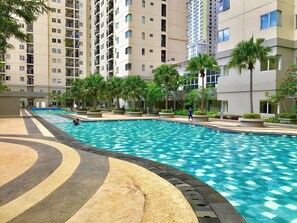 A swimming pool surrounded by a landscaped area with palm trees and a high-rise building in the background.