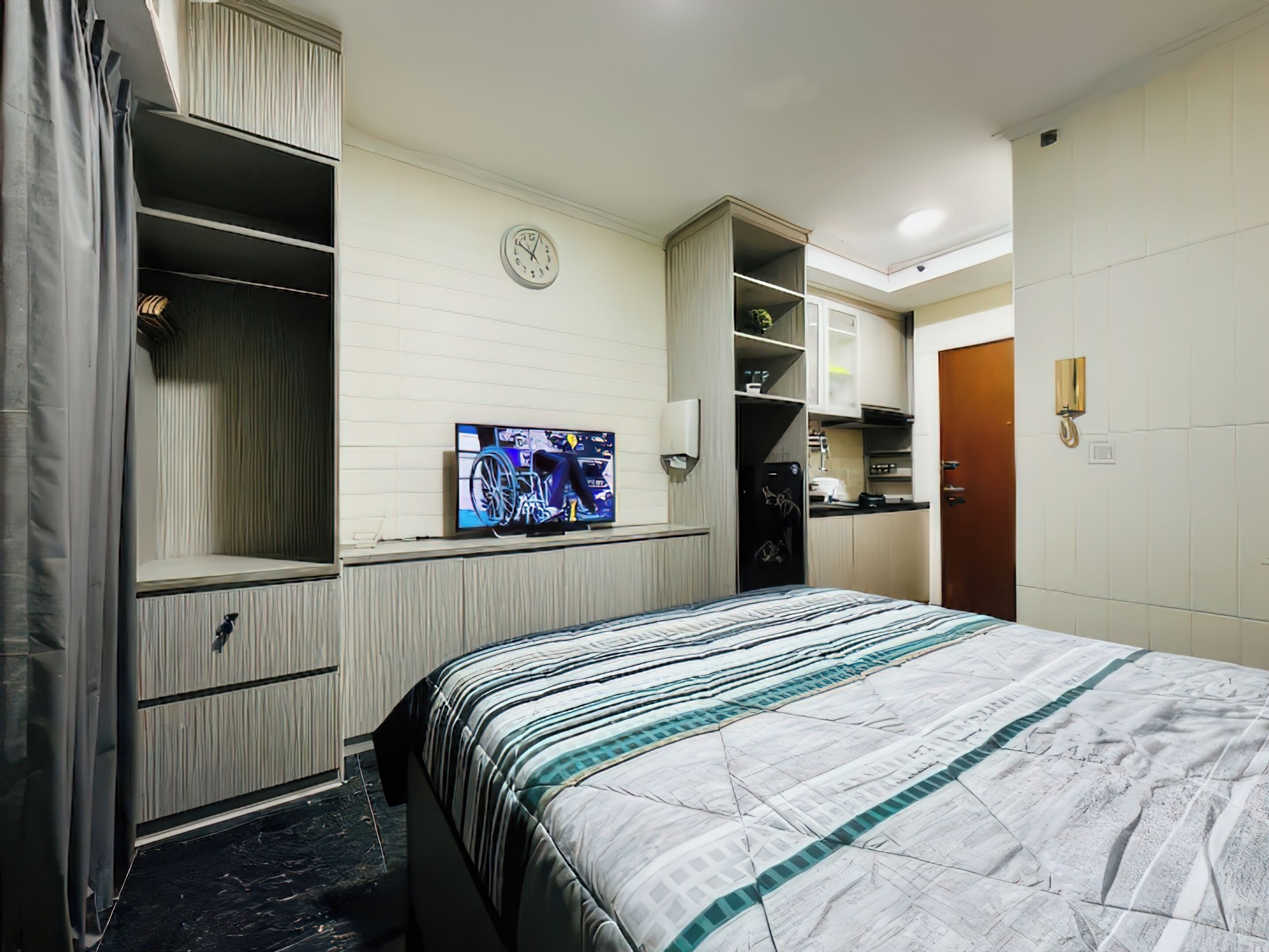 A hotel room with a bed, a television, a wardrobe, and a small kitchenette.
