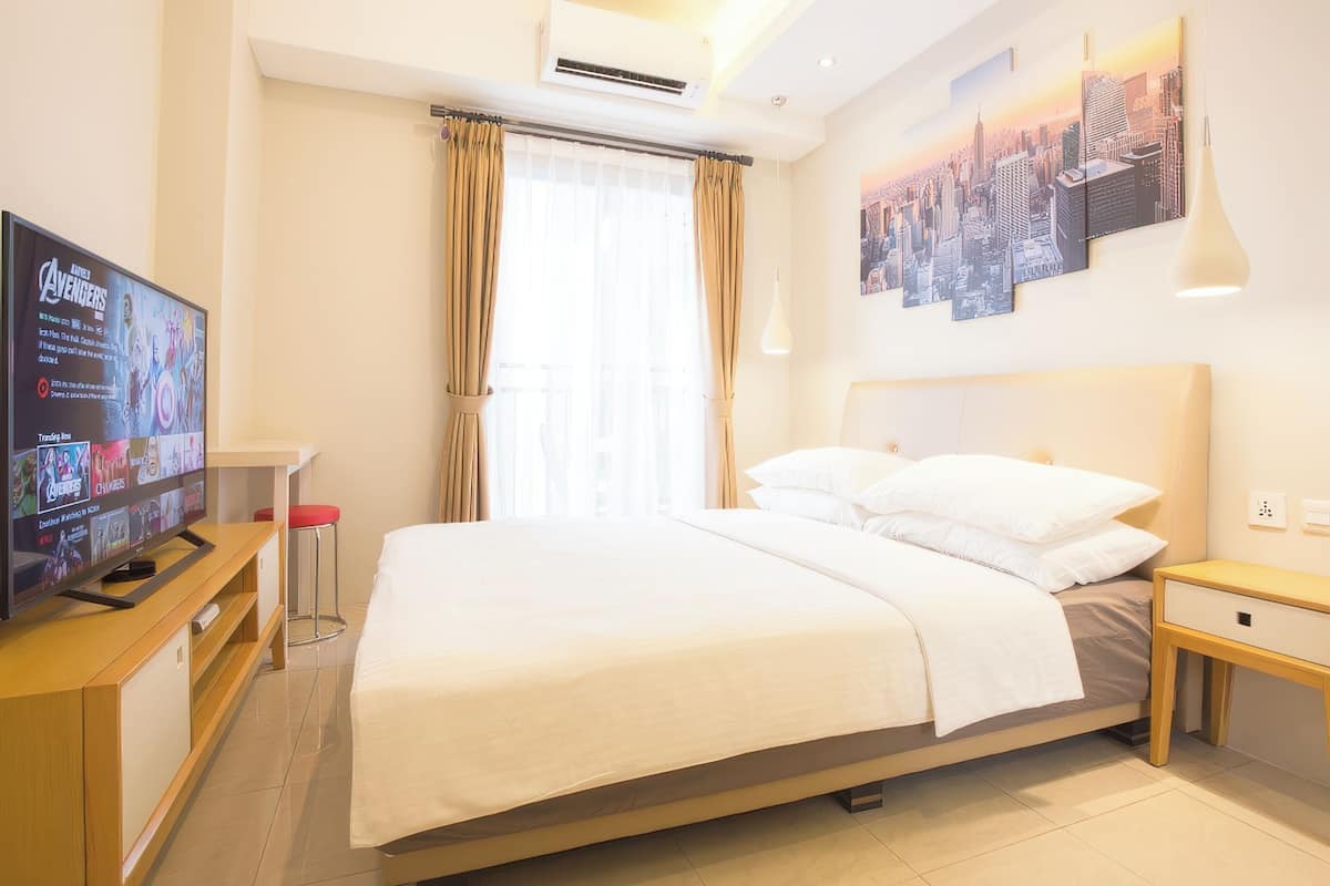 Ein Hotelzimmer mit einem Bett, einem Fernseher, einem Stadtbild-Kunstwerk und einem Fenster mit Vorhängen.