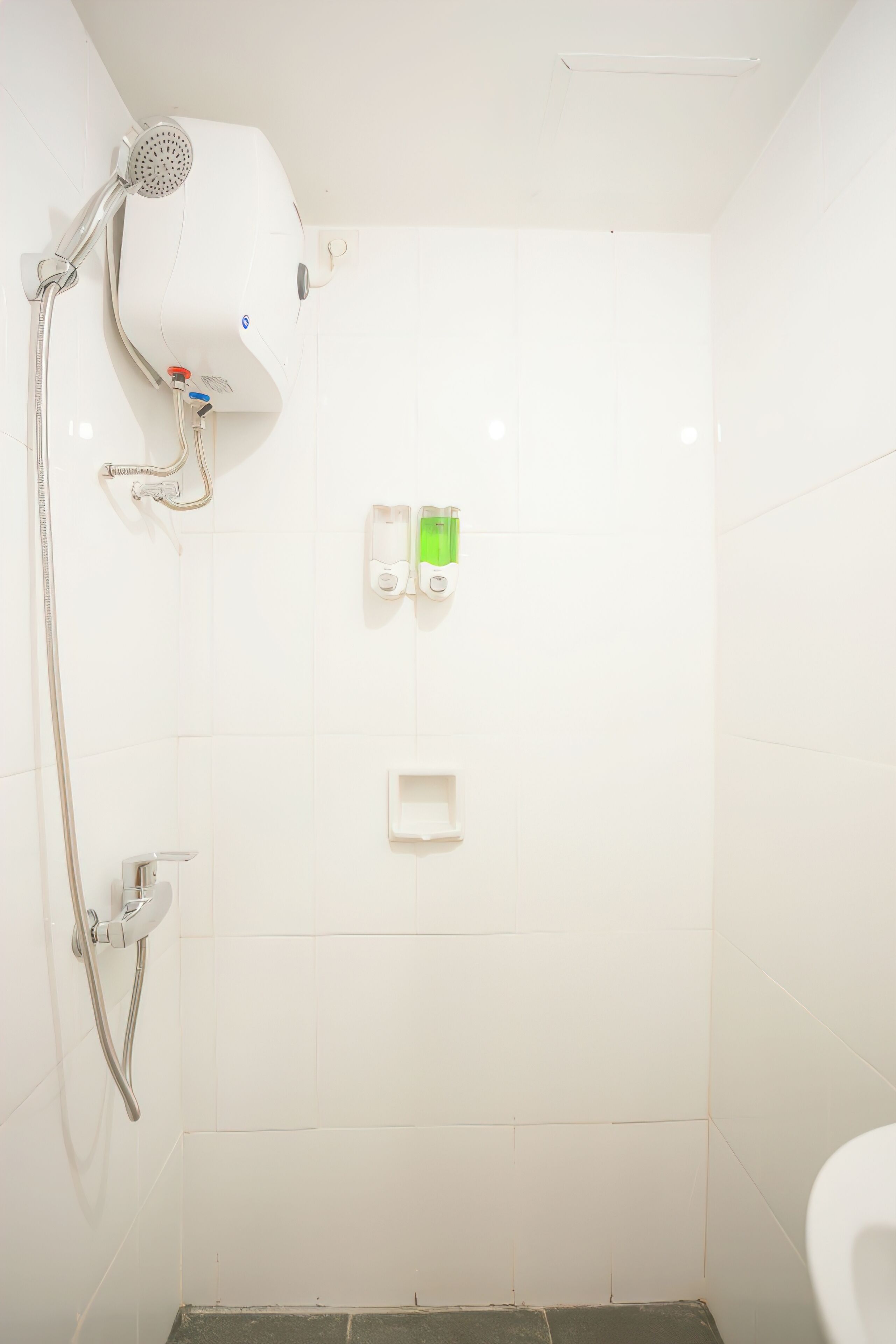 Área de duche com chuveiro manual, painel de controlo na parede e dispensador de sabonete.