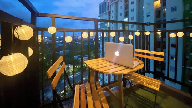 Ein Balkon mit Holztisch und Stühlen, einem Laptop und Papierlampen.