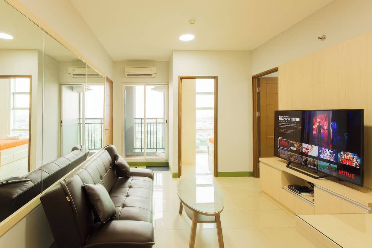 Ein modernes Wohnzimmer mit Ledersofa, Glastisch und Flachbildfernseher auf einer Holzablage.