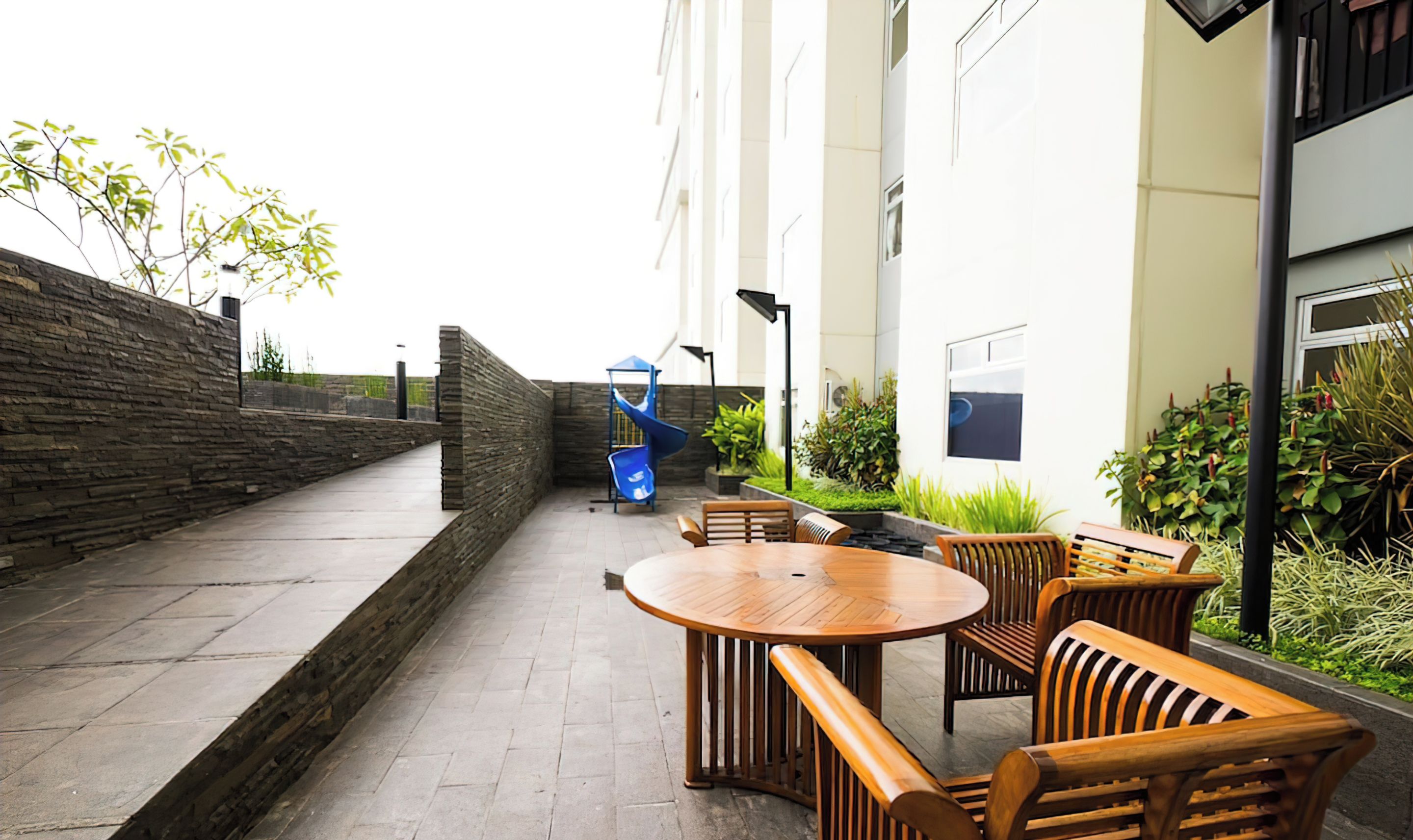 An outdoor patio with a round wooden table and chairs, a blue chair, and a small blue trash bin.