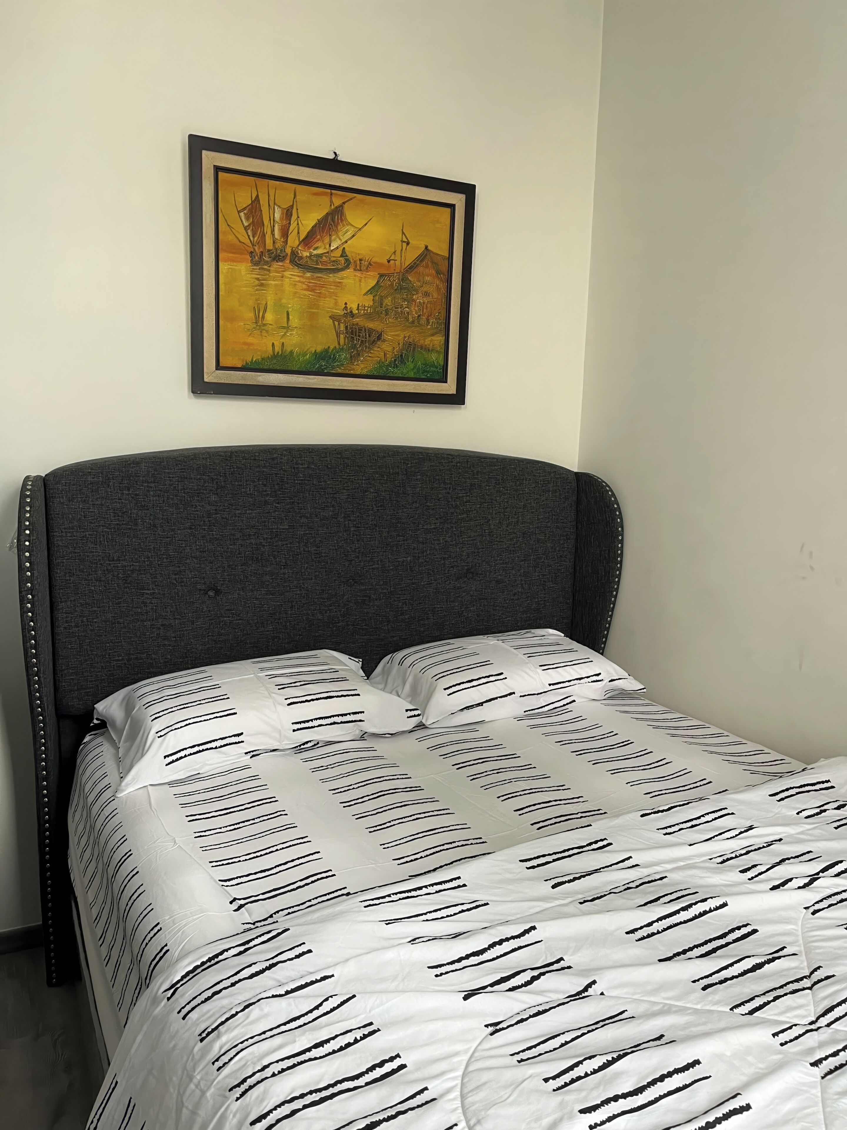 A bed with a grey upholstered headboard and white bedding with black stripes.
