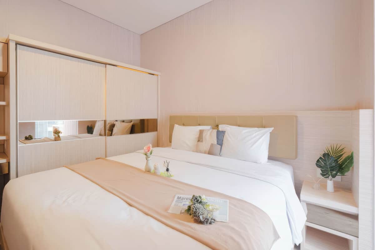 Quarto de hotel com uma cama grande, um guarda-roupa, uma mesa de cabeceira com uma planta e um espelho.