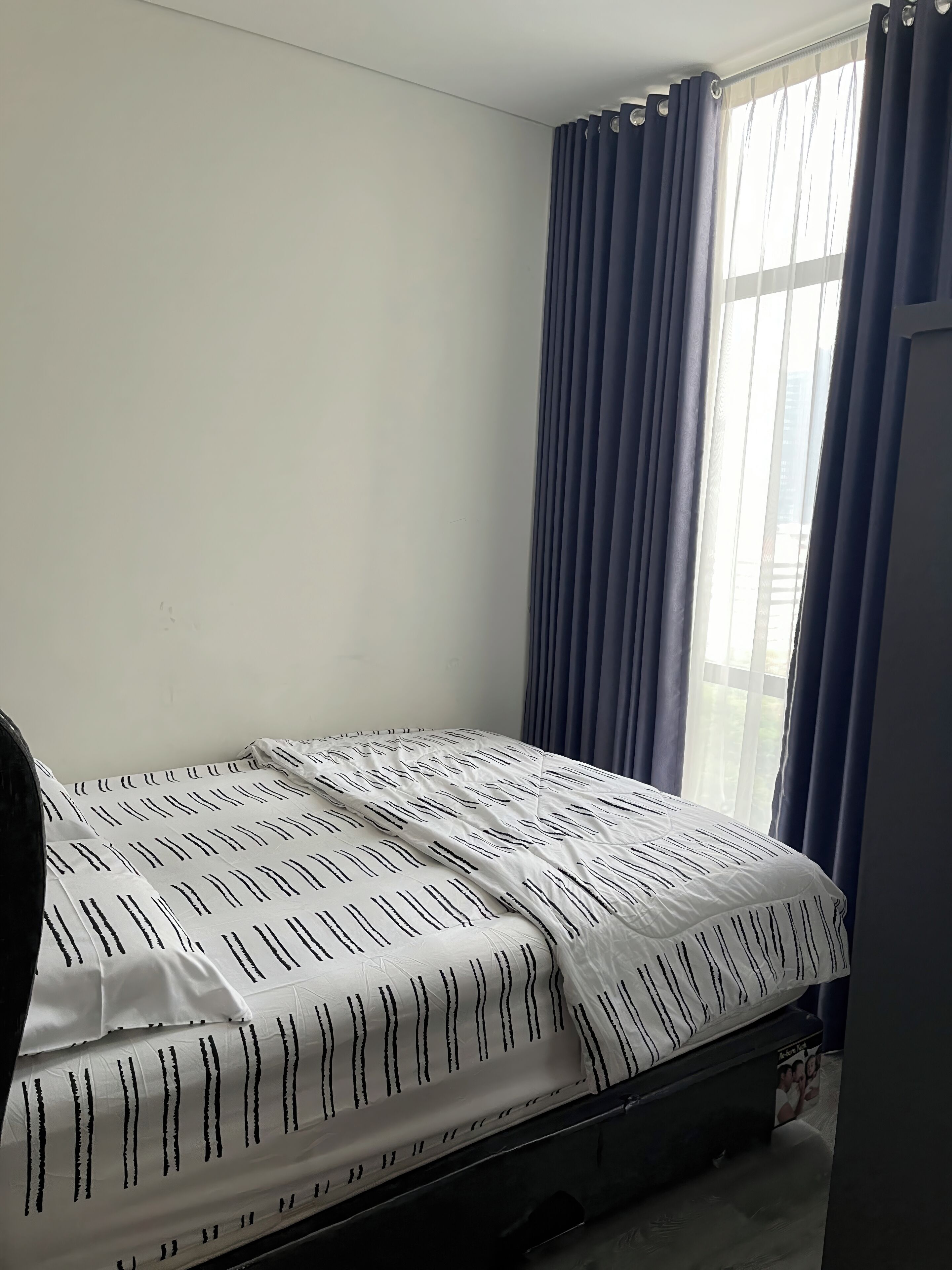 Un dormitorio con cama, ventana con cortinas y pared lisa.