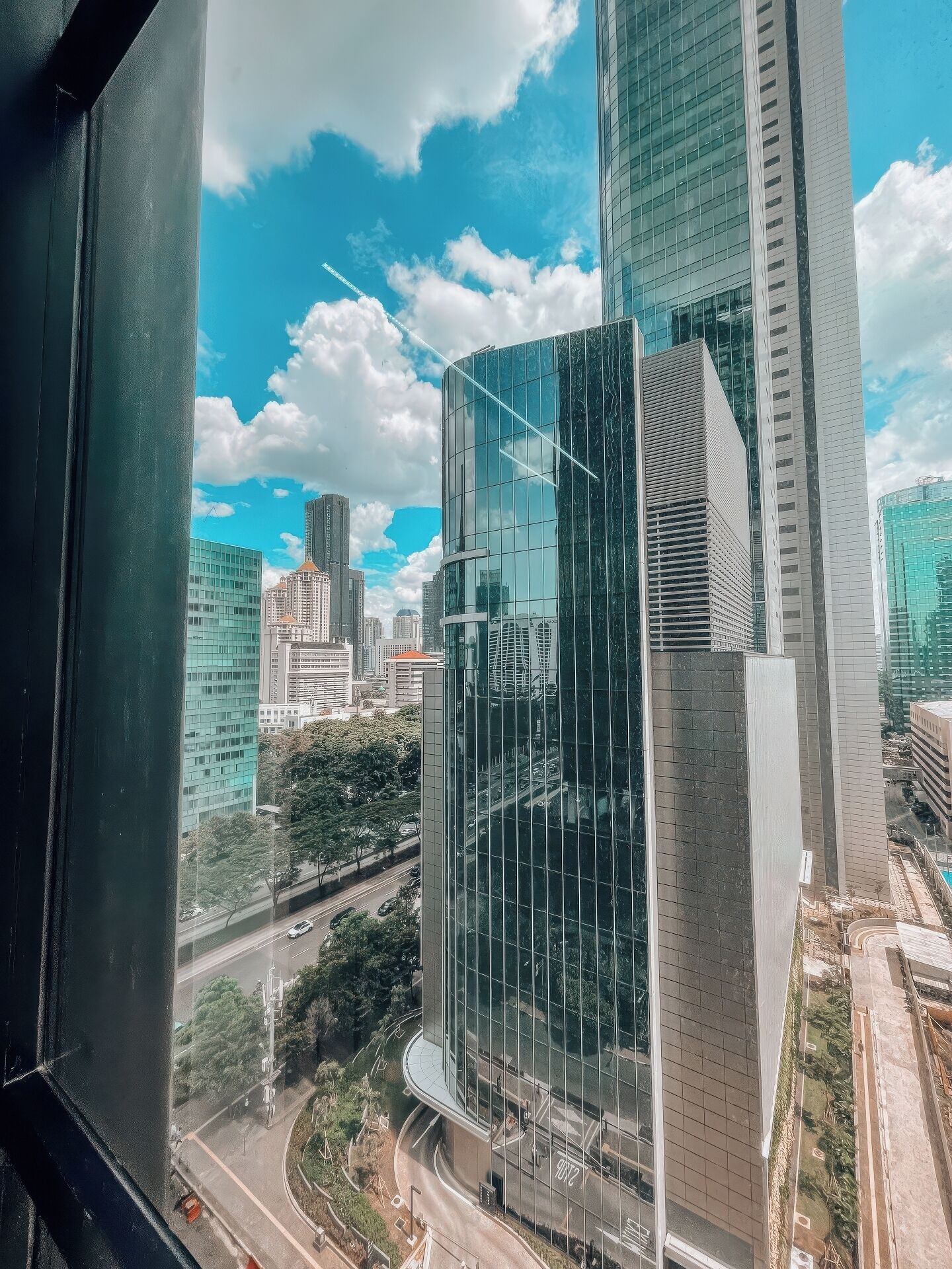 A modern high-rise building with a glass facade, surrounded by other tall buildings and a clear blue sky.
