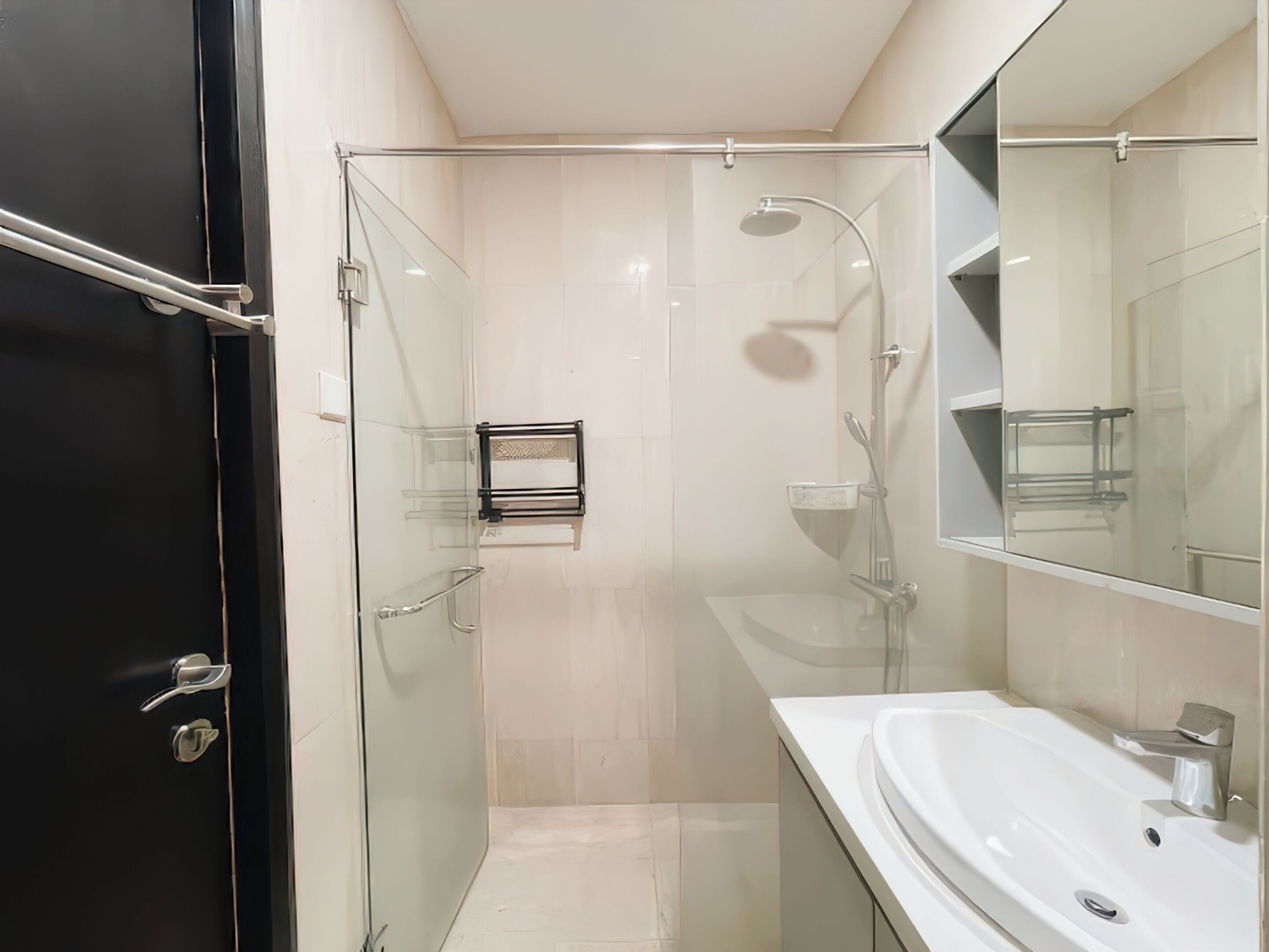 A modern bathroom with a glass-enclosed shower, a white sink, and a black door.
