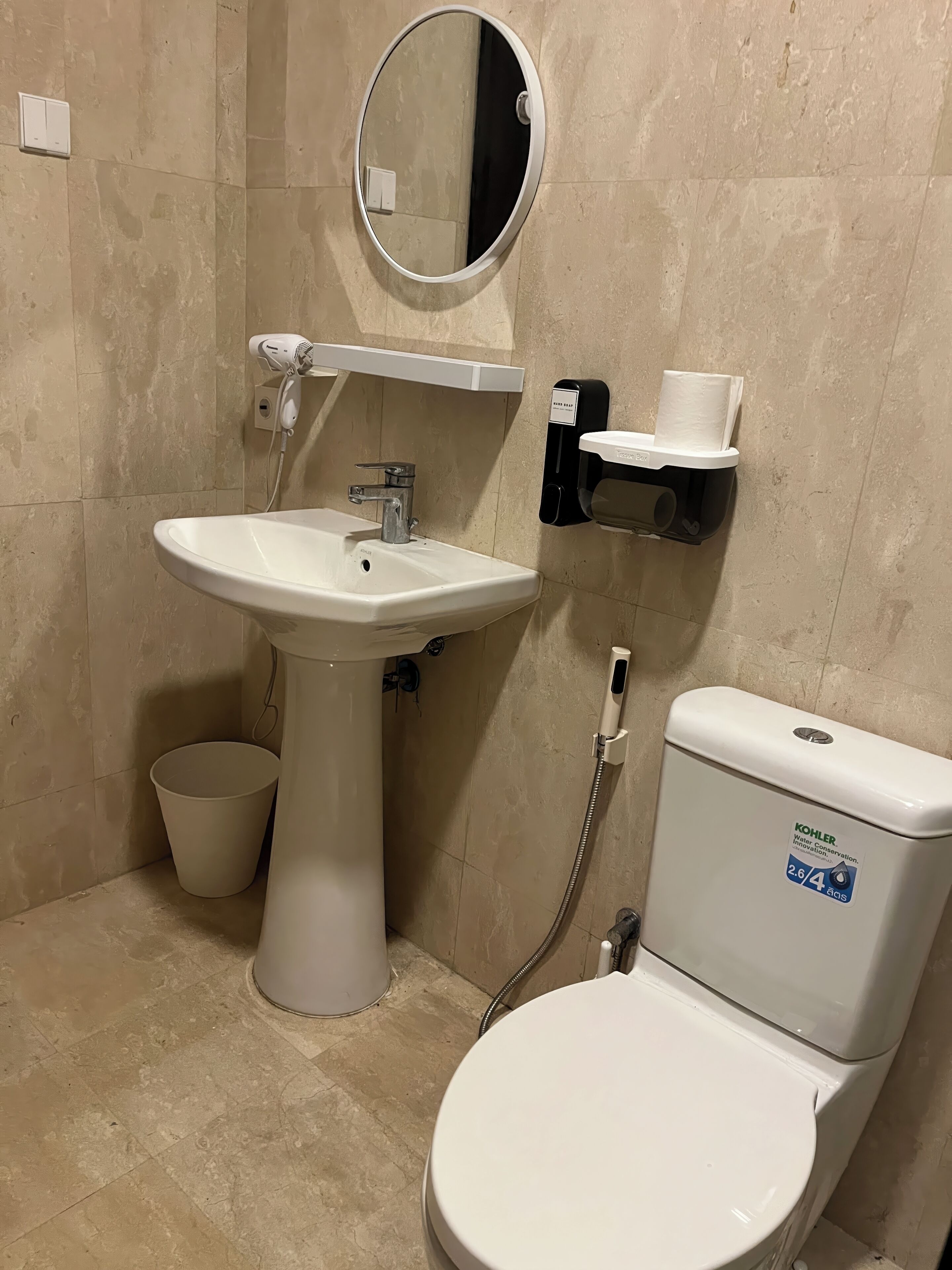 A bathroom with a white sink, toilet, and a towel dispenser.