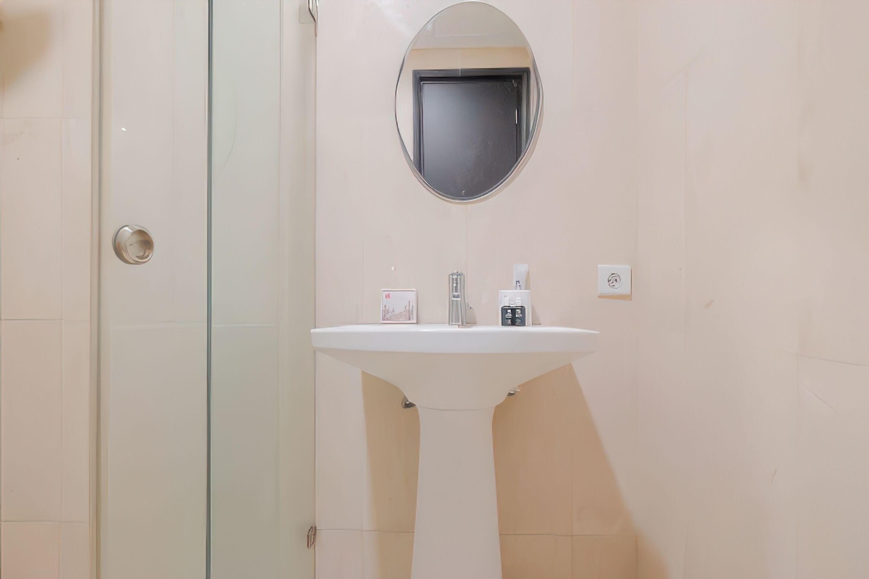 Ein Badezimmer mit einem weißen Waschbecken, einem runden Spiegel und einer Duschkabine aus Glas.