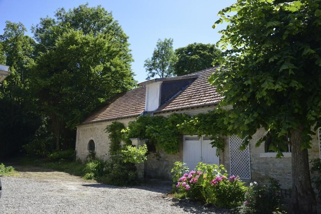 A rustic stone building with a tiled roof, surrounded by lush greenery and flowering plants.