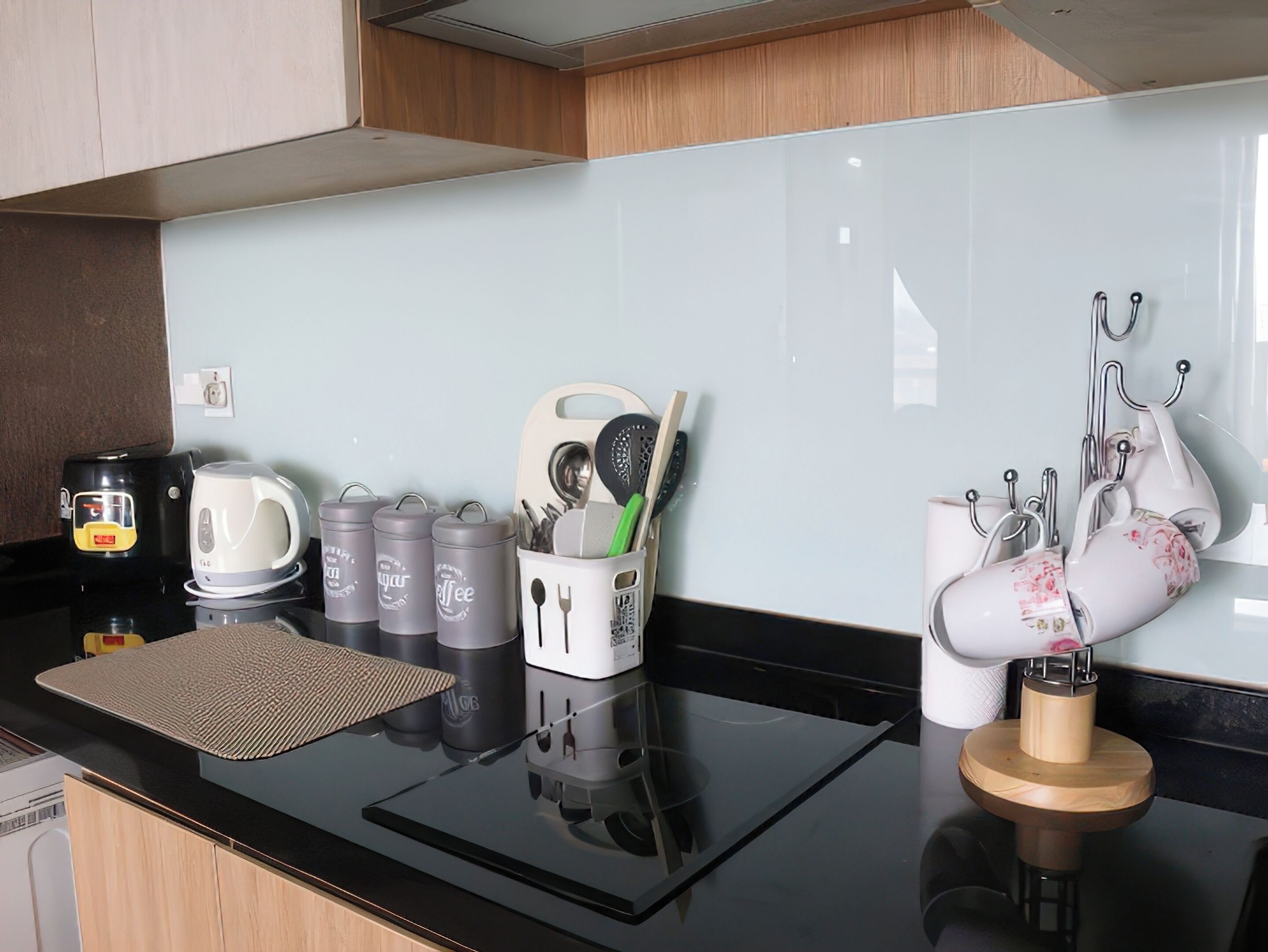 A modern kitchen with a black countertop, a coffee machine, a kettle, and a tea kettle. There are also utensils and a knife block on the wall.