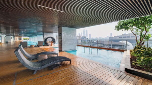 Un espace piscine intérieur moderne, doté de chaises longues, offrant une vue sur les gratte-ciel de la ville et comprenant une partie couverte avec un plancher en bois.