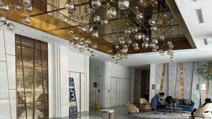 Un hall d’entrée spacieux doté d’un sol en marbre, d’un plafond haut orné de luminaires sphériques suspendus et d’un espace détente avec des canapés et des tables.