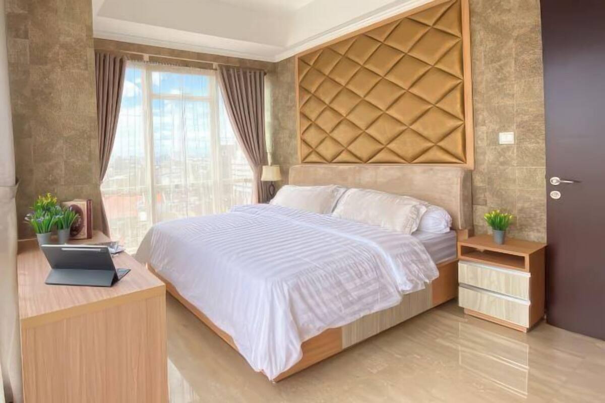 Une chambre à coucher moderne avec un lit, un bureau avec un ordinateur portable, une table de chevet et une plante en pot.