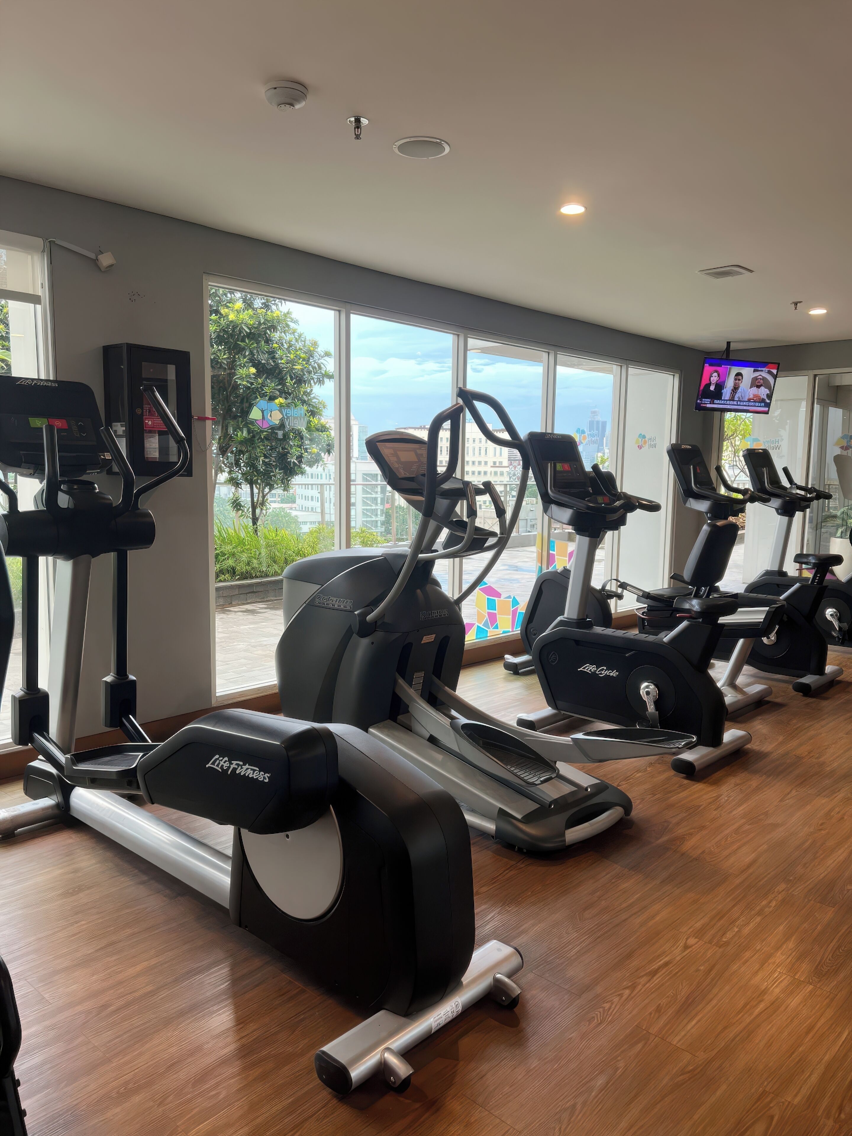 Ein Fitnessstudio mit mehreren Laufbändern, Ergometer und einem Fernsehbildschirm, der einen Nachrichtensender zeigt.