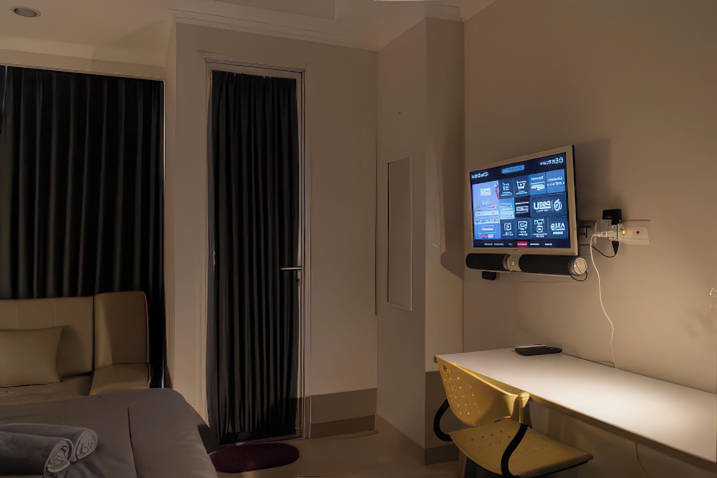 Ein Hotelzimmer mit einem Bett, einem Schreibtisch, einem an der Wand befestigten Fernseher und einer Tür mit Vorhängen.