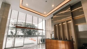 A modern lobby with a reception desk, large windows, and a geometric floor pattern. - Staycation Jakarta Holland Village (Jakarta)