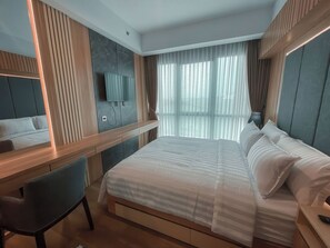 A modern hotel room with a large bed, a desk, a chair, a TV, and a window with sheer curtains. - Staycation Jakarta Holland Village (Jakarta)