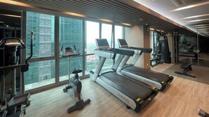 A modern gym with treadmills, stationary bikes, and a rowing machine. Large windows offer a view of the cityscape. - Staycation Jakarta Holland Village (Jakarta)