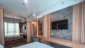 A modern hotel room with a large bed, a desk, a chair, a TV mounted on a marble wall, and a mirror. - Staycation Jakarta Holland Village (Jakarta)