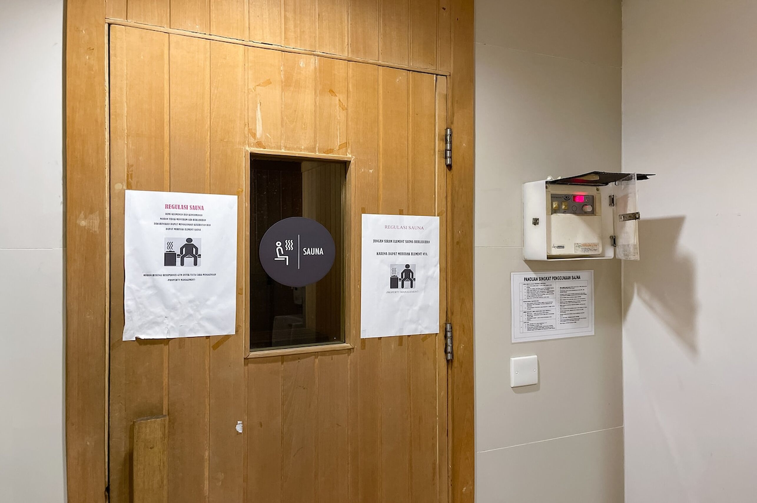 A wooden door with a sauna sign and a control panel on the wall.