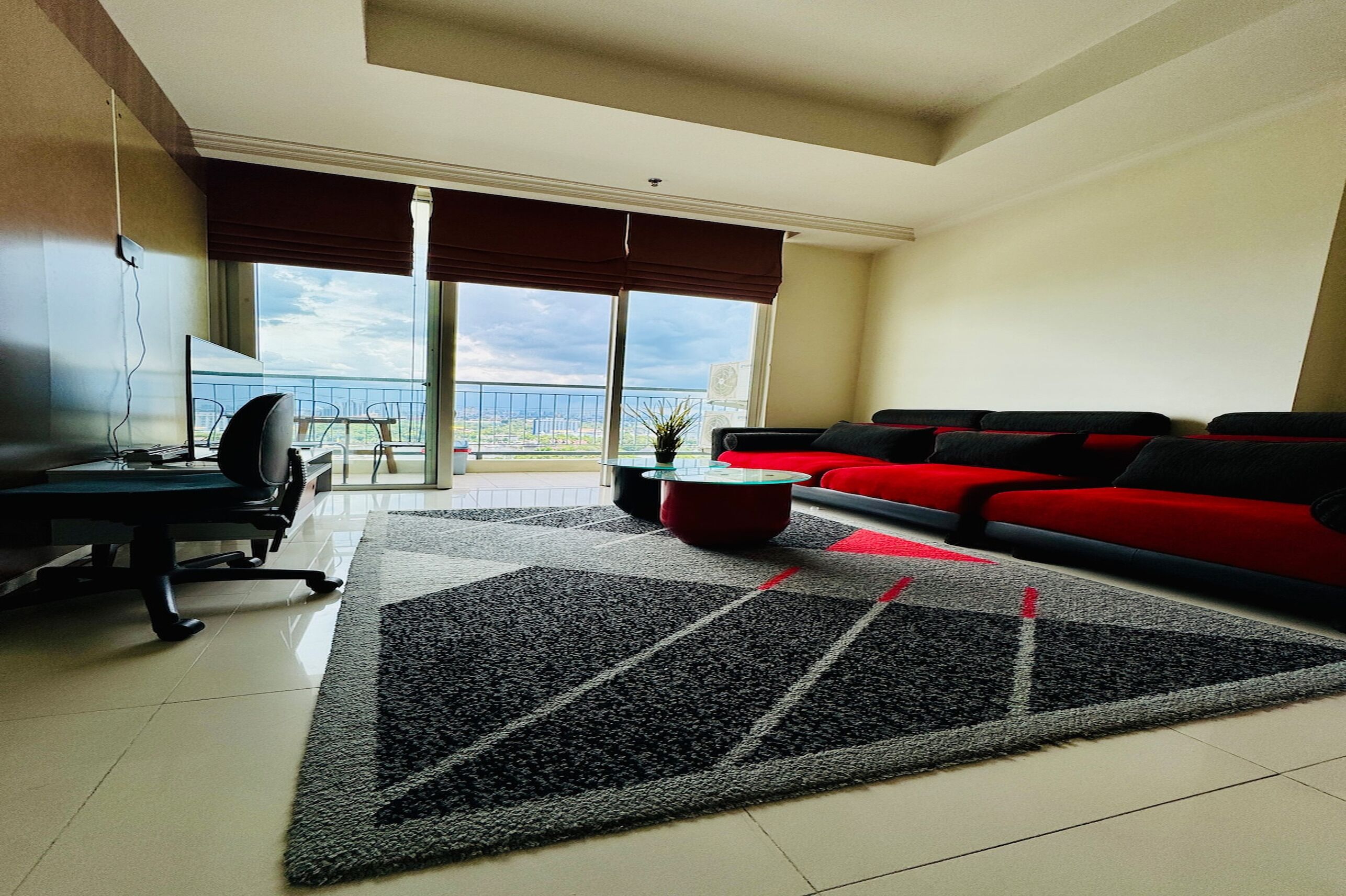 A modern living room with a red sofa, a black and white rug, a small coffee table, and a TV on a desk.