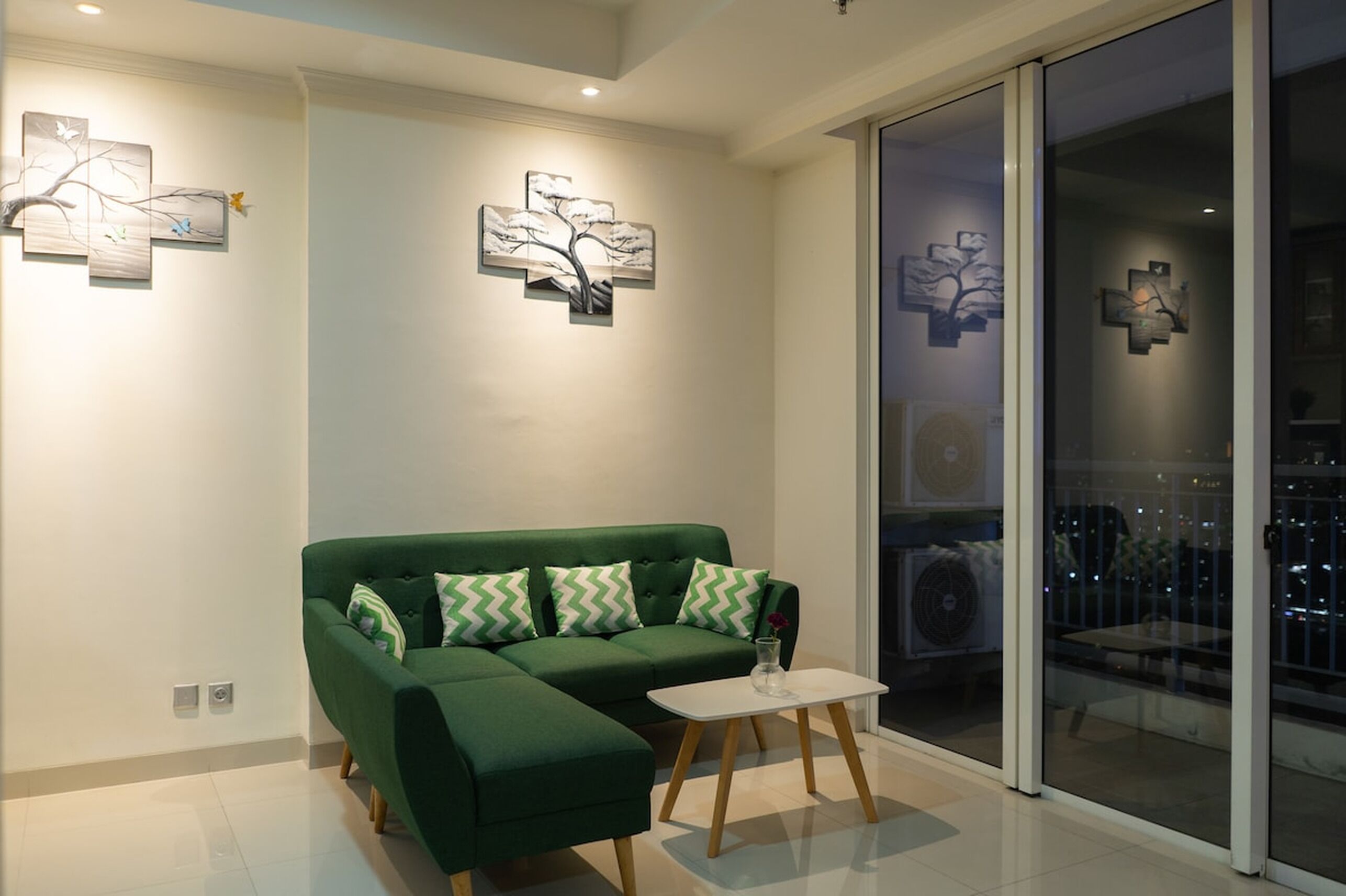 A modern living room with a green sectional sofa, a small white table, and artwork on the walls.