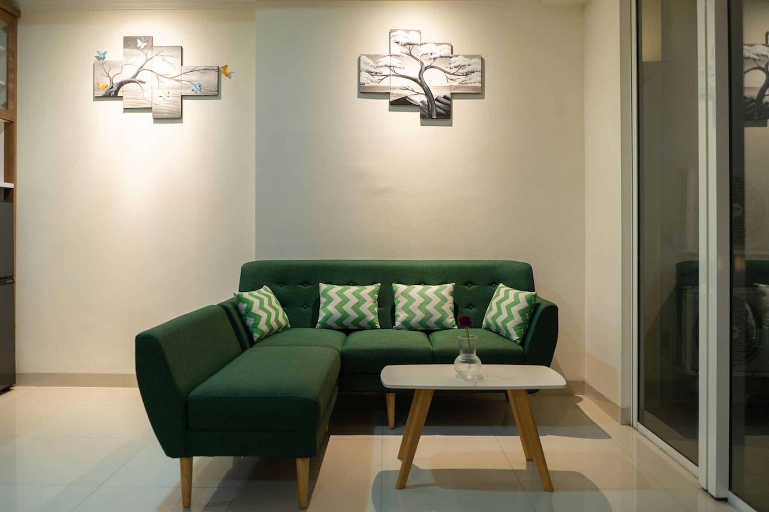 Een groene bank met houten poten, een witte bijzettafel en twee wanddecoraties.