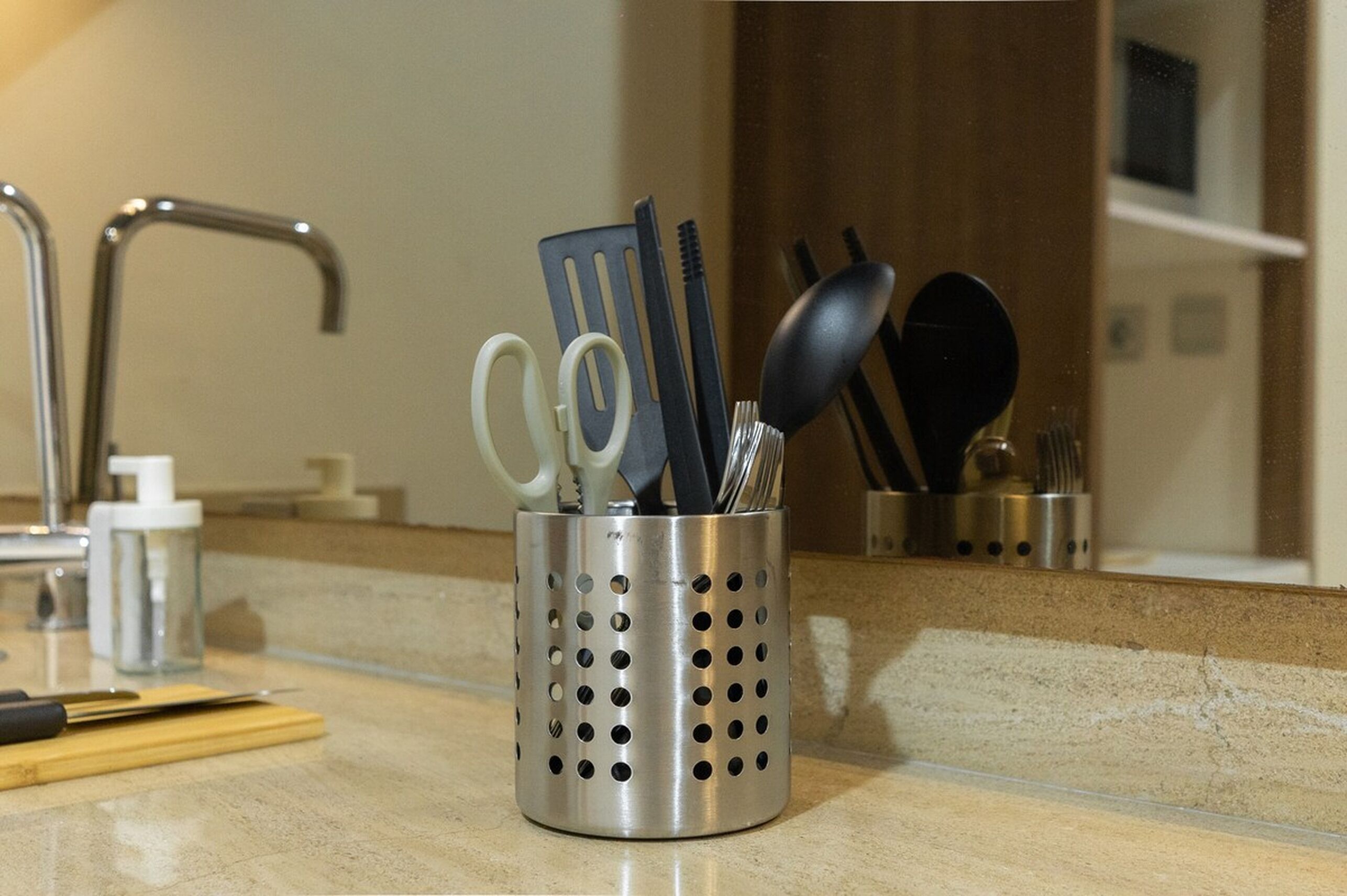 Un plan de travail de cuisine avec un porte-ustensiles en acier inoxydable contenant des ciseaux, une spatule et une cuillère.