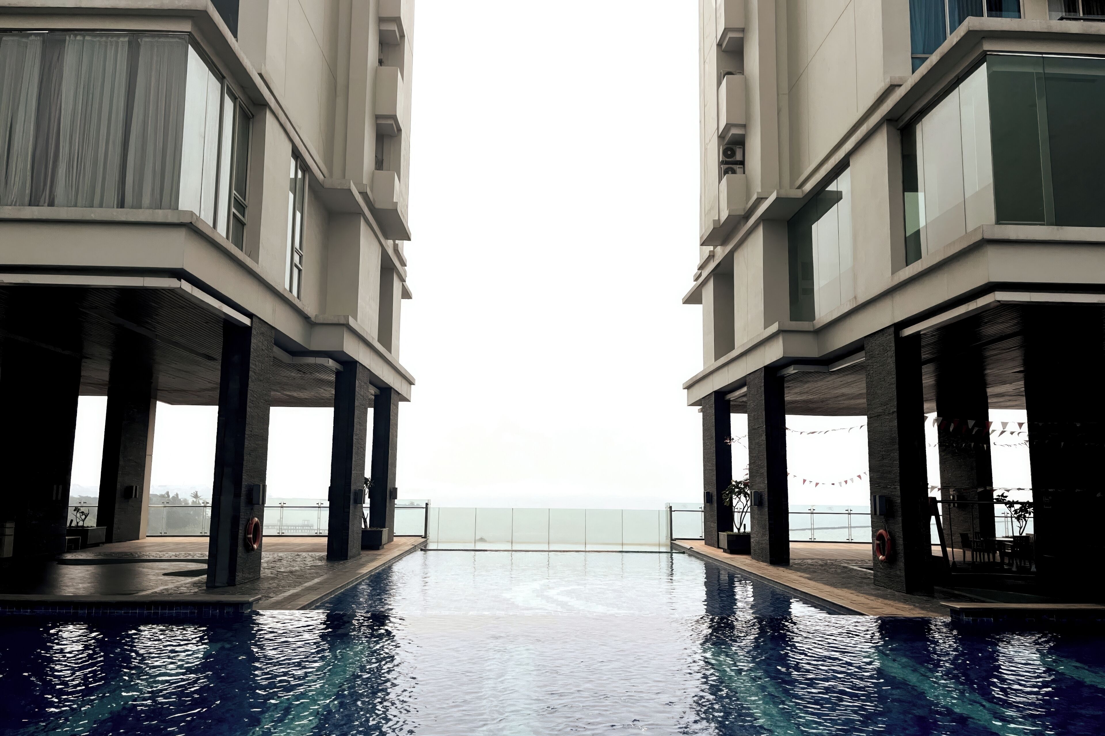 Un hotel moderno con piscina central, grandes ventanales y vista al mar.