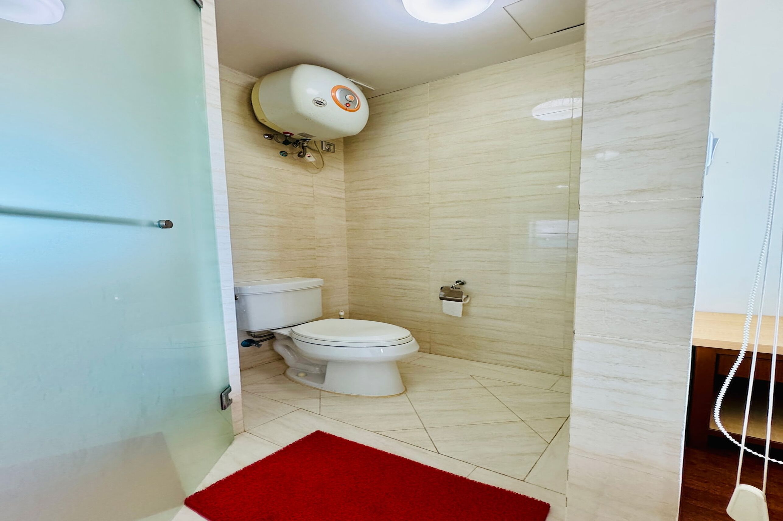 Une salle de bain avec des toilettes, une douche et un tapis rouge.