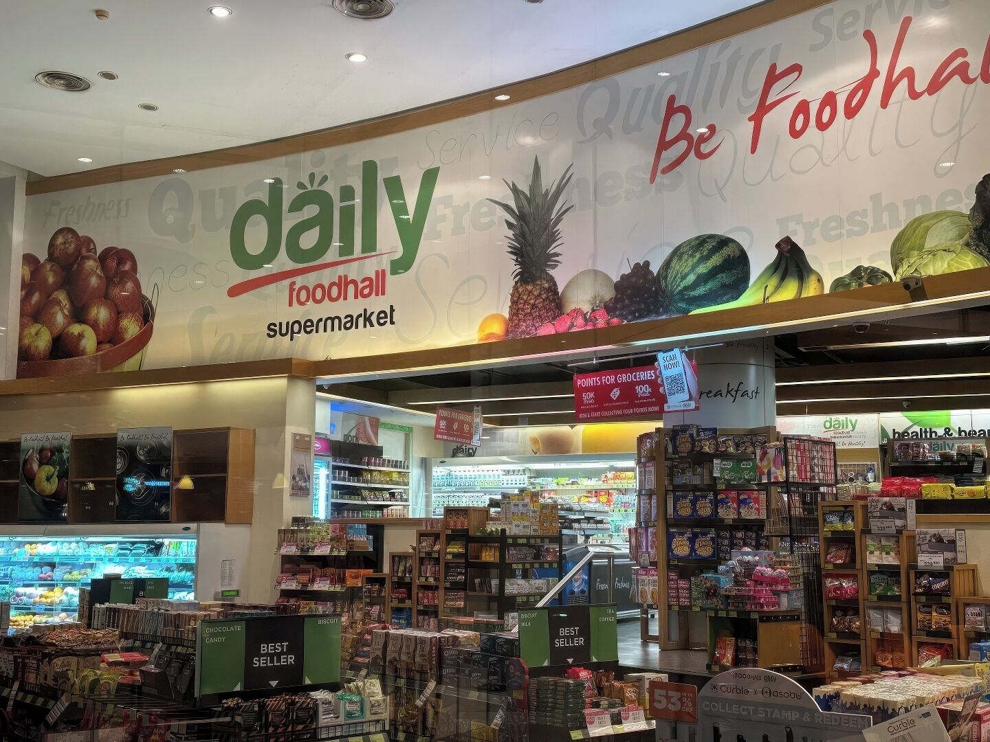 A supermarket interior with a large sign reading "daily foodhall supermarket" and various product displays.