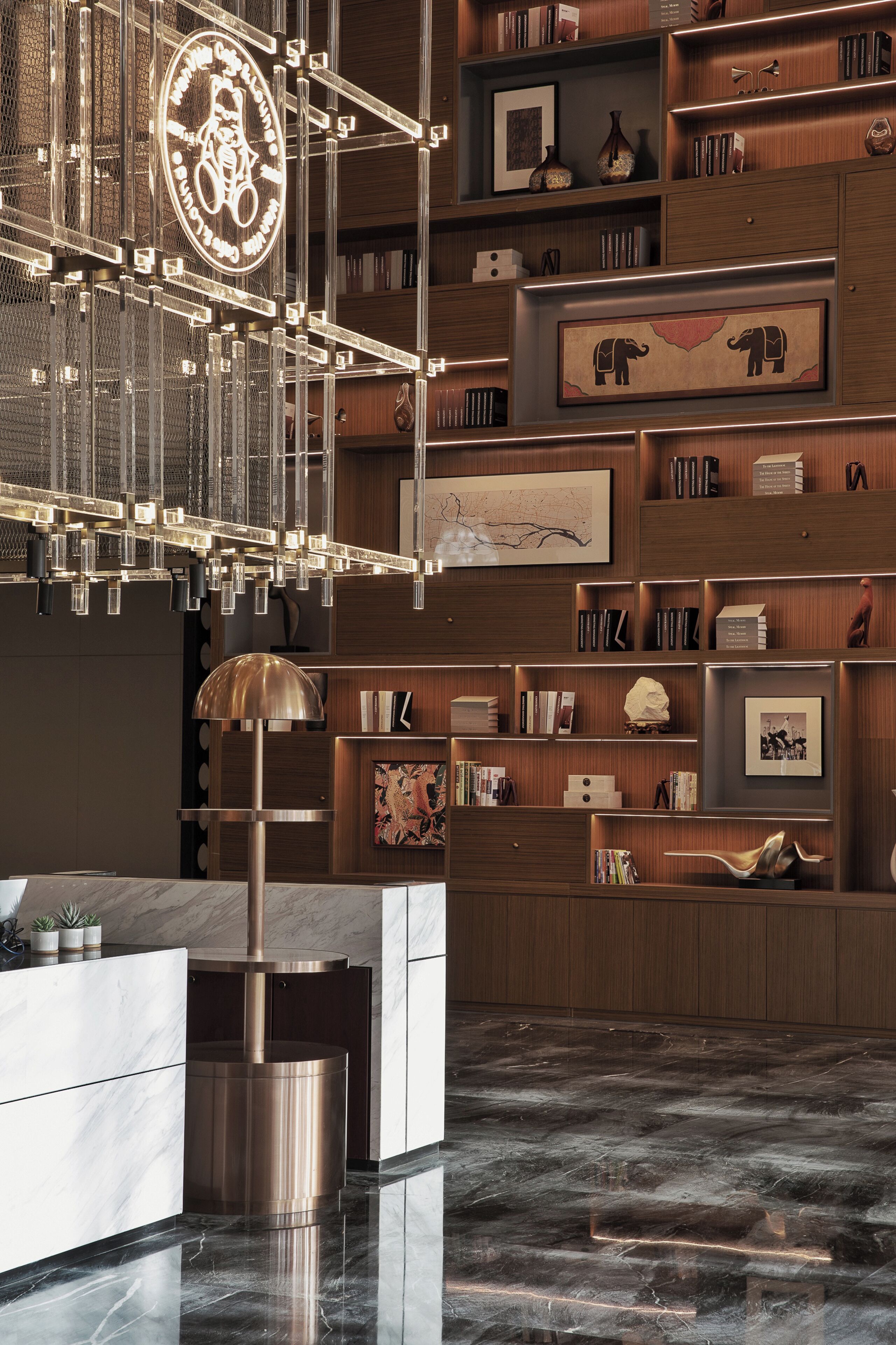 A modern interior with a marble reception desk, a large chandelier, and wooden shelving with books and decorative items.