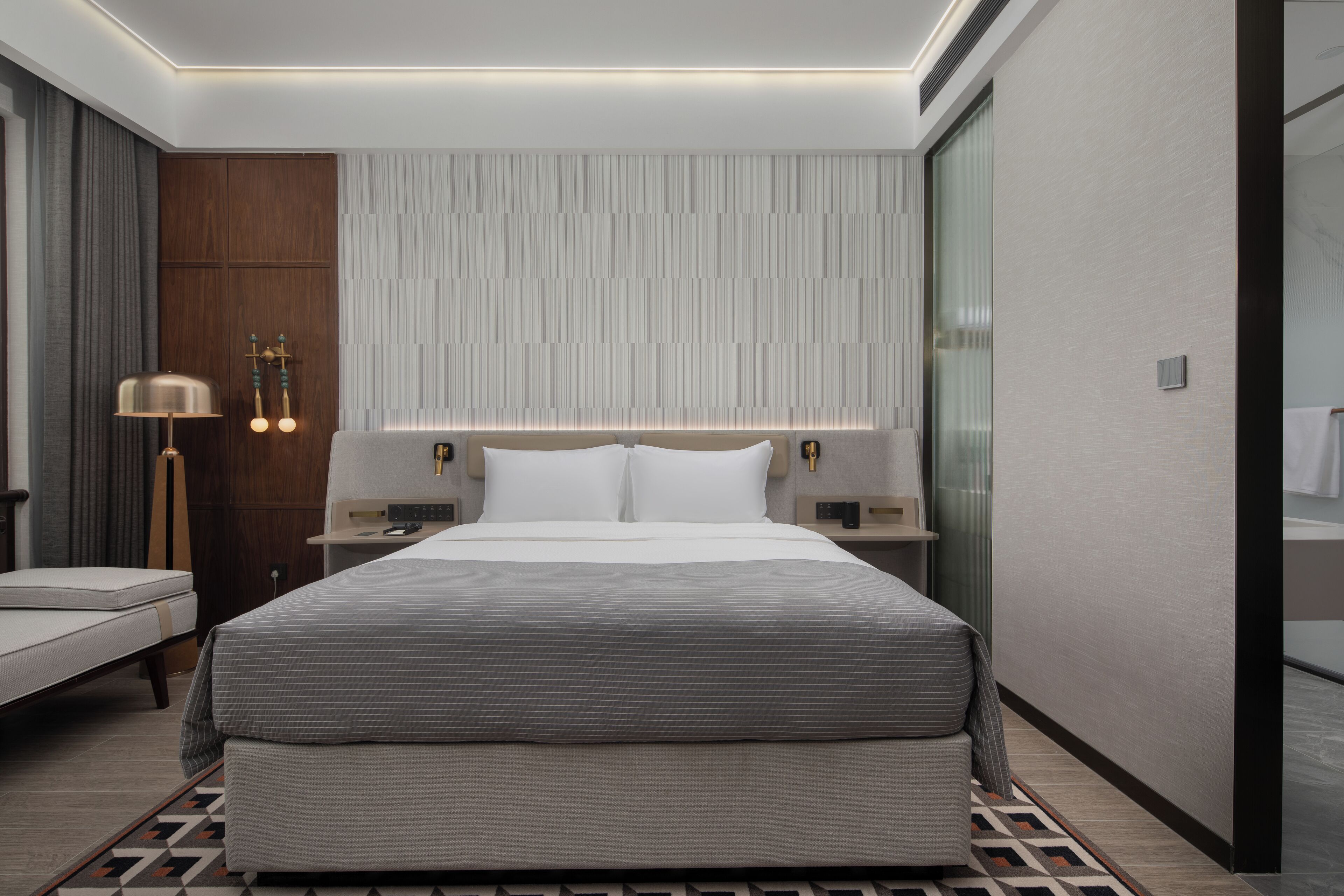 Een moderne hotelkamer met een groot bed, nachtkastjes, een lamp en uitzicht op de stad.